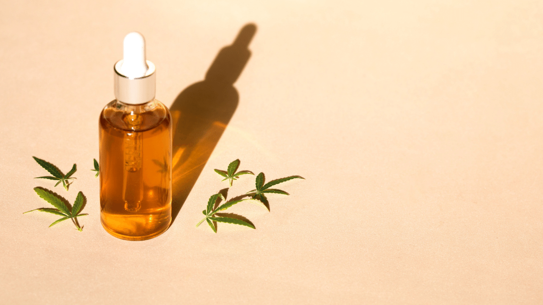 Bottle of oil with small hemp leaves on a peach colored background